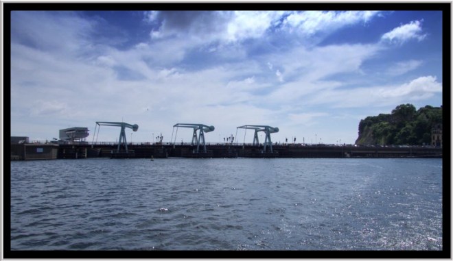 The barrage from the water showing the lock gates and cranes that lift the road way to allow boats in and out..