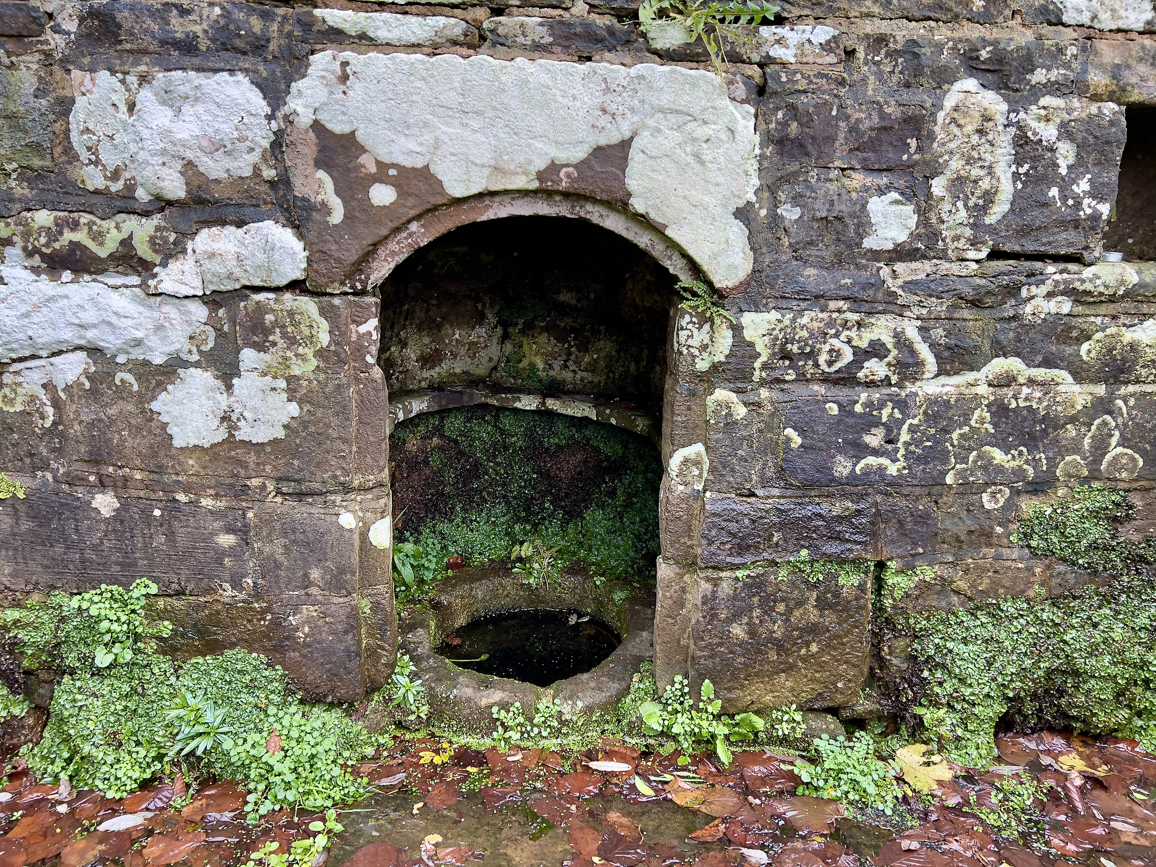 The well water is captured in a small stone bowl, allowing easy access to those who need to do so.